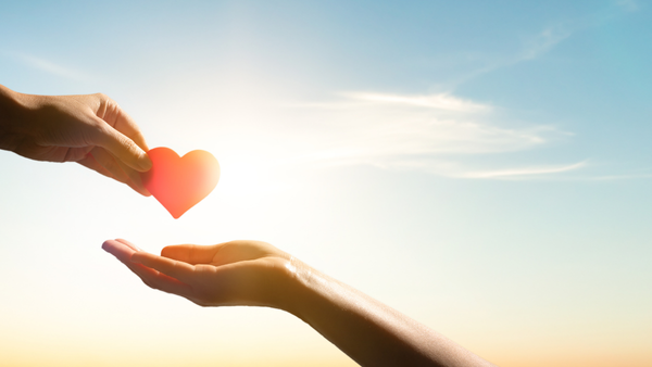 An outstretched hand offers a heart to another
