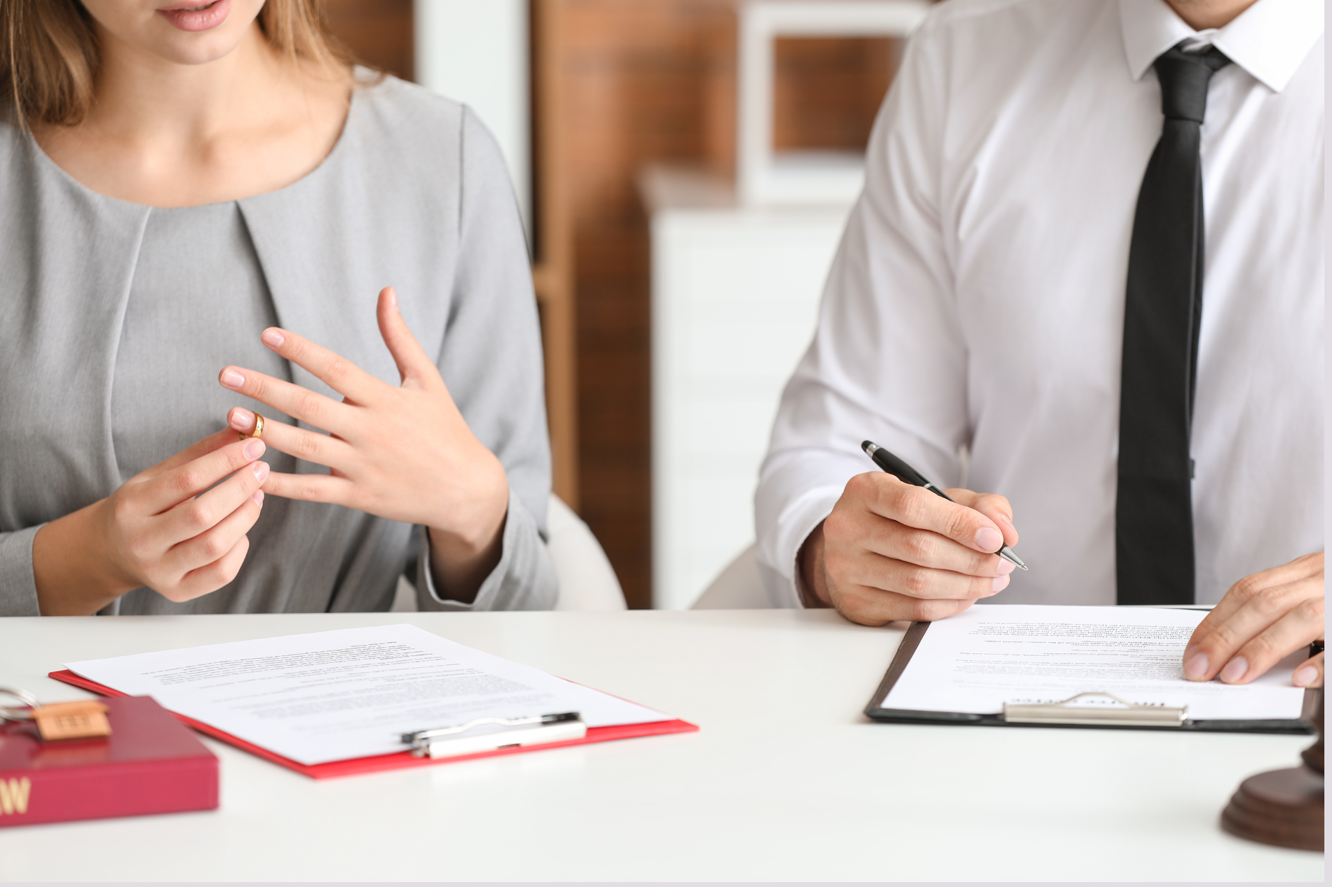 Woman and man sitting down ready to sign divorce papers and taking off their rings