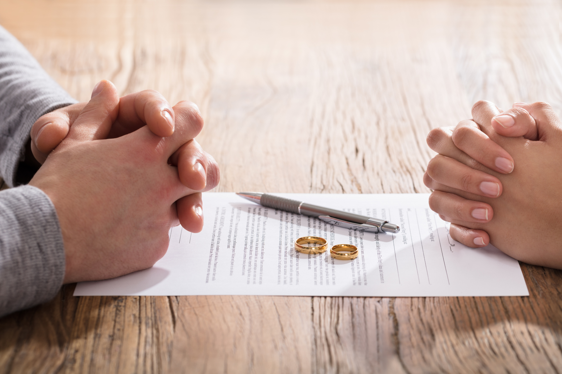 two people sitting across from one another with divorce papers and wedding bands in the middle
